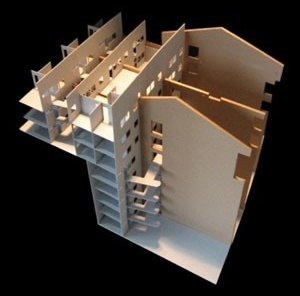 Vista da maquete em construção onde se nota a implantação da proposta sobre a estrutura preexistência (o terreno em dois níveis separados por uma contenção e as paredes divisórias entre as quatro casas), bem como os pátios internos e as passarelas<br />Imagem dos autores do projeto 