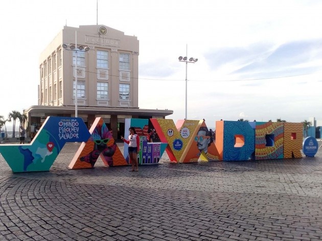 Letreiro "Salvador" na frente do Elevador Lacerda, com a inscrição na primeira letra: “Carnaval 2019 – O mundo escolheu Salvador”. Outras letras contêm imagens de máscaras carnavalescas, fachadas coloridas das casas coloniais, retrato de Castro Alves<br />Foto Volha Yermalayeva Franco 