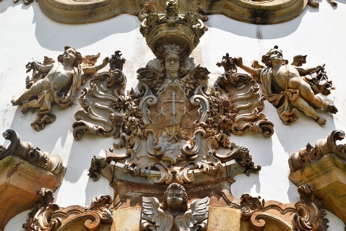 Brasão da Ordem do Carmo ladeado por dois querubins esvoaçantes e encimado pela cabeça de um terceiro, sustentando a coroa da Virgem, motivo central da portada da Igreja de Nossa Senhora do Carmo, Aleijadinho (atribuição), Ouro Preto MG, 2014<br />Foto Elio Moroni Filho 