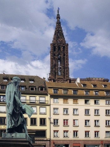Estátua de Gutenberg segurando nas mãos uma página do primeiro livro impresso em Mainz – a Bíblia – onde está escrito: “Et la lumière fut”; ao fundo, torre da Catedral de Notre-Dame de Strassbourg<br />Foto Victor Hugo Mori 