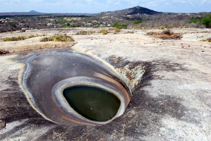 Foto 1 - O lajedo, circundado pelo cariri tendo, ao fundo, elevações isoladas e, em primeiro plano, um pequeno lago quase seco