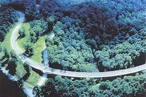 Os pilares dessa estrutura de concreto “desaparecem” visualmente abaixo do nível da vegetação; e a pista parece flutuar no plano verde da superfície das copas das árvores. Parece que os projetistas da estrada quiseram, além da minimização do impacto dessa [ISTEA. Landscape Architecture, March 1985, p 47]