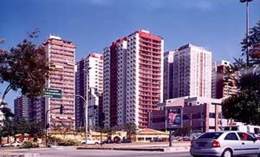 Paisagem da Barra da Tijuca, com o paredão resultante das "torres em meio ao verde", cada um em seu condomínio fortemente cercado, por detrás de faixa de comércio (shopping mall) e de via expressa, onde as distâncias são dificilmente precorridas por pedes