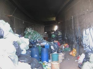 Vista do espaço de trabalho da Assoc. PE 2. Mesas e bombonas rodeadas por lixo que será triado